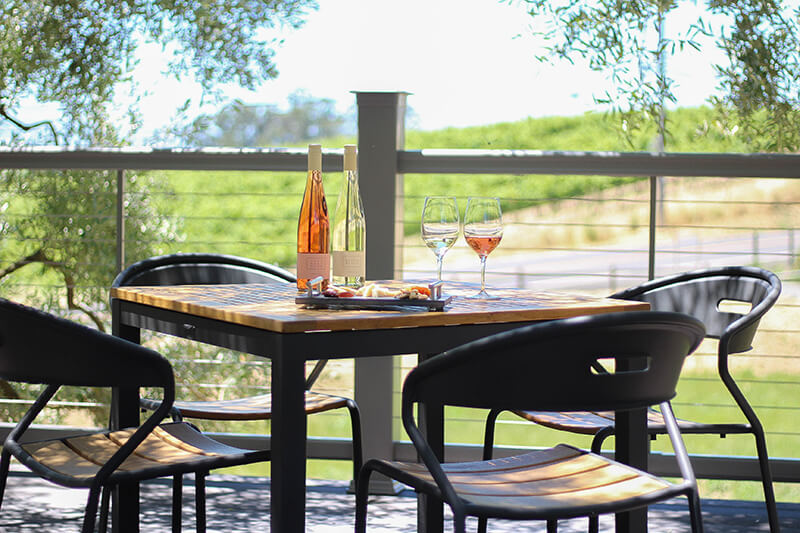 A bottle of red and white wine with glasses on a table in front of a vineyard