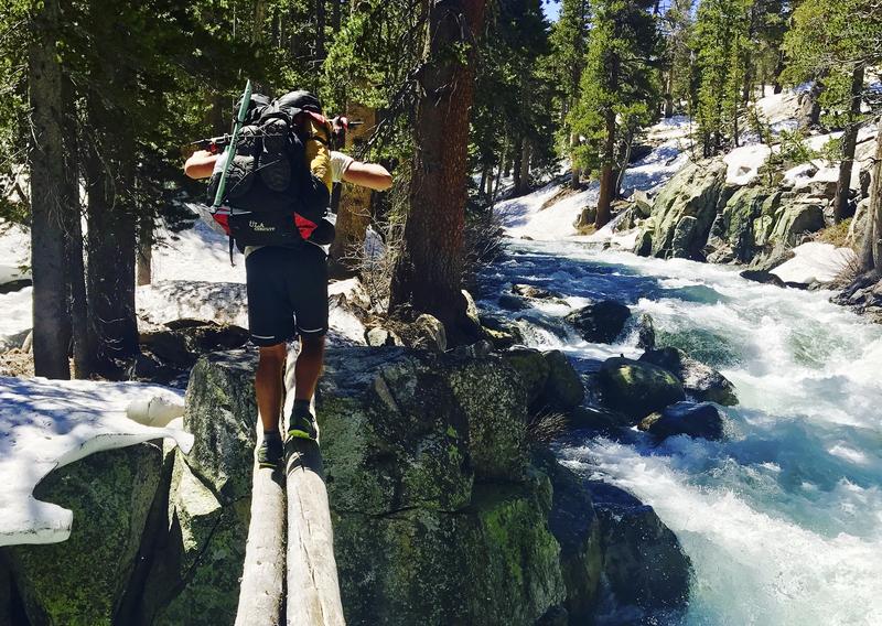 man walking on a log over a river in the woods