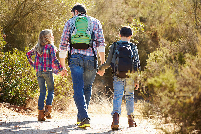 dad and children holding hands and hiking in the woods