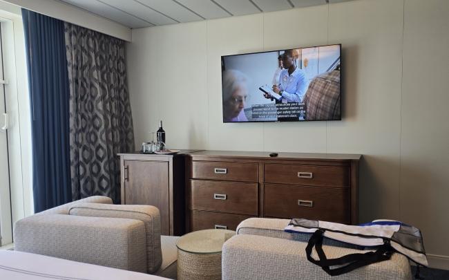 The dresser area of #423, a Veranda Suite, on American Serenade. It has plenty of storage drawers, a nice flat top surface, a wall-mounted, flat-screen TV above, and a mini-fridge.