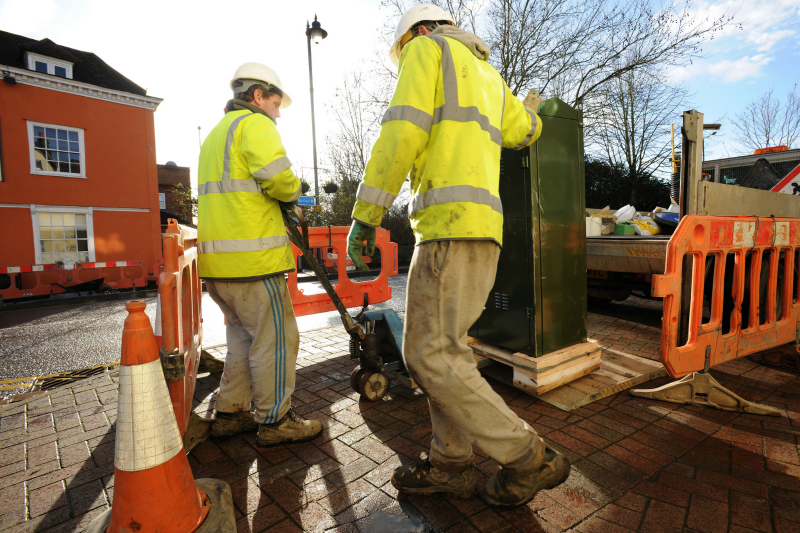two utility workers setting up a fiber cabinet on a sidewalk