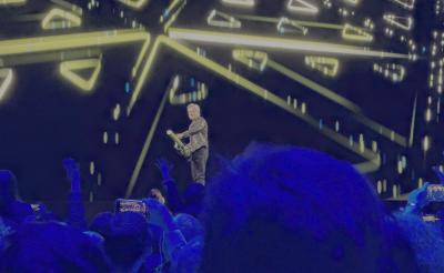 A small figure of a man on a distant stage gleefully wields a T-shirt gun