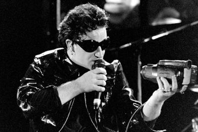 Bono on stage in 1993 singing into a handheld video camera.
