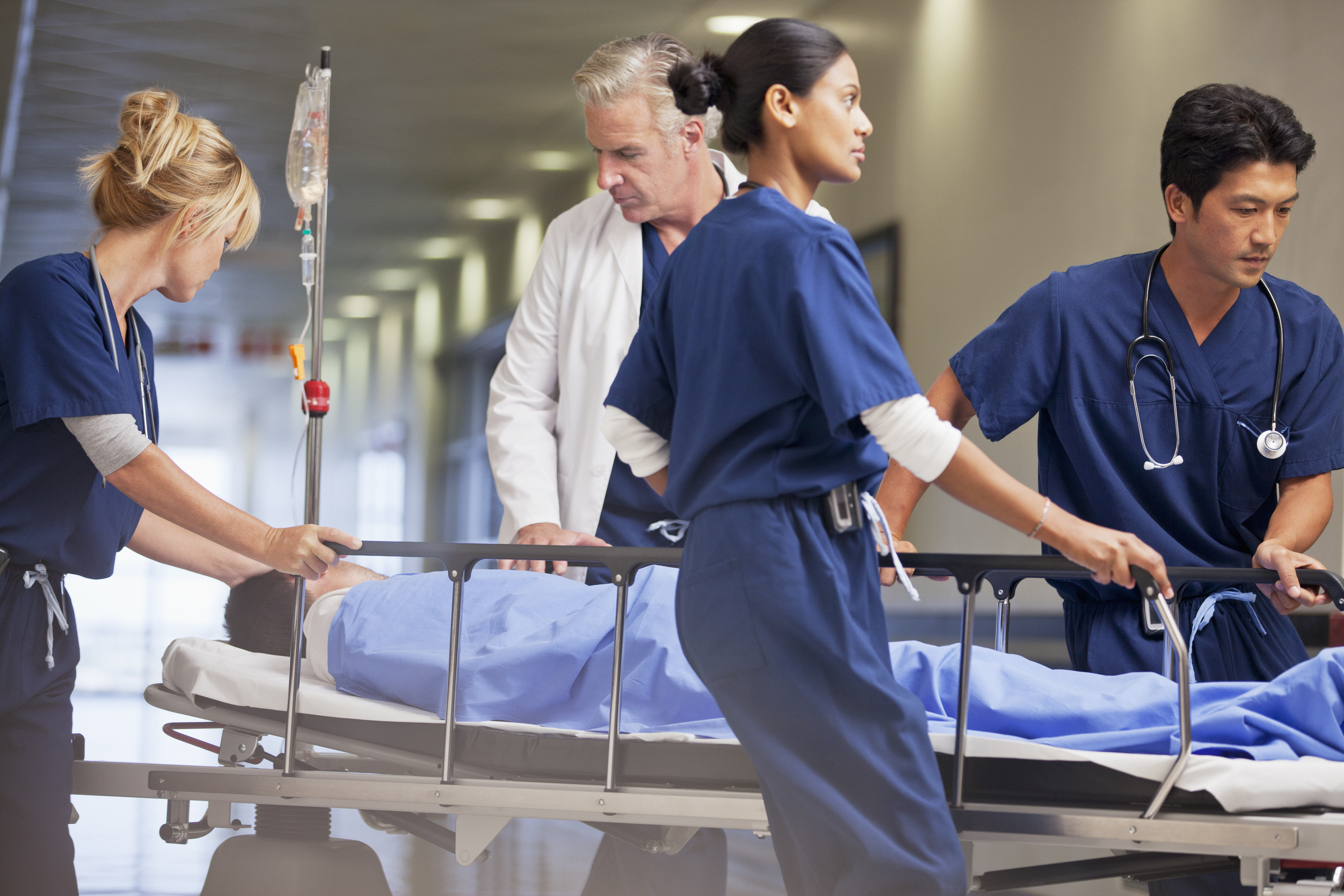 Doctor and nurses wheeling patient in gurney through hospital corridor