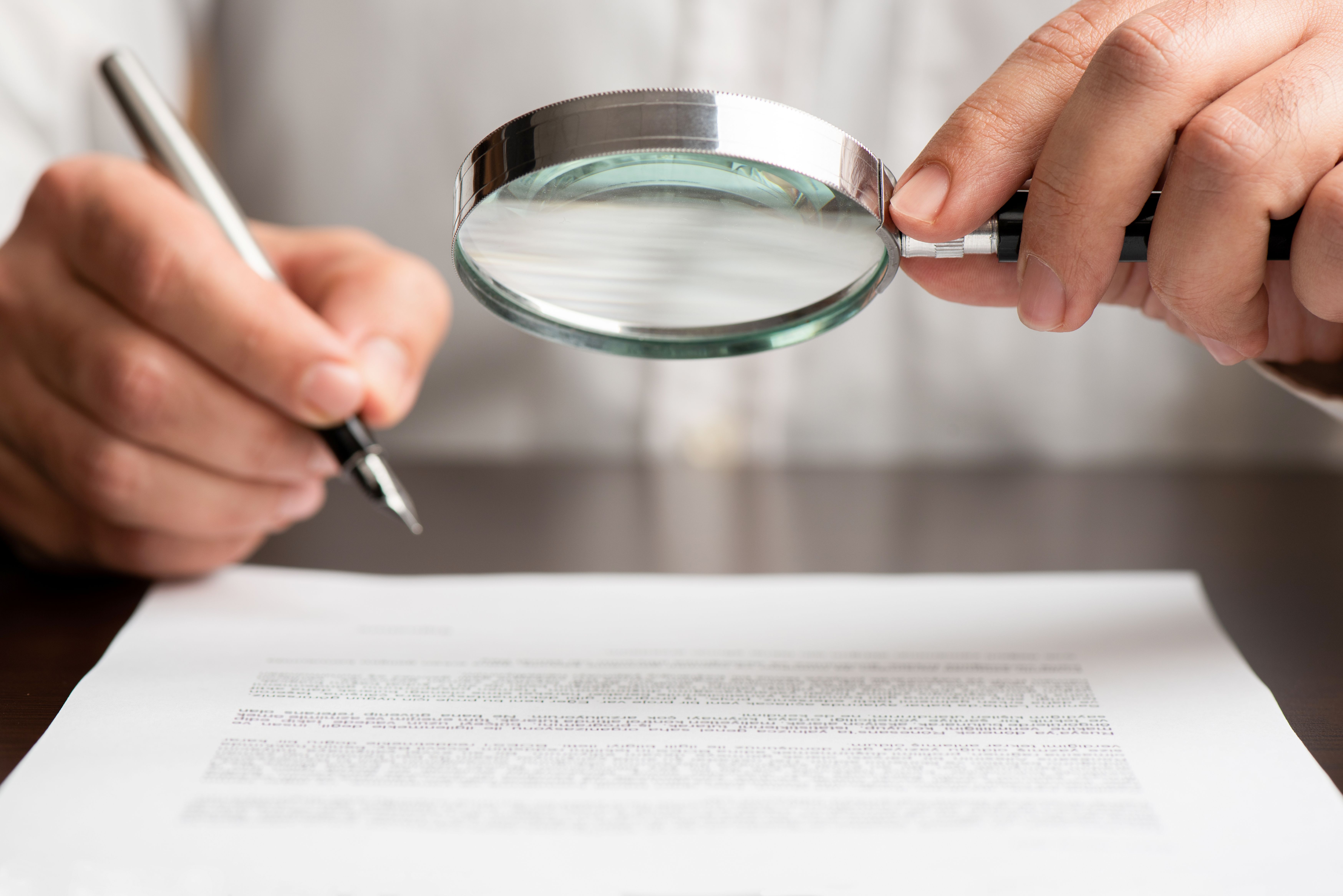 Man scrutinizing printed text with a magnifying glass
