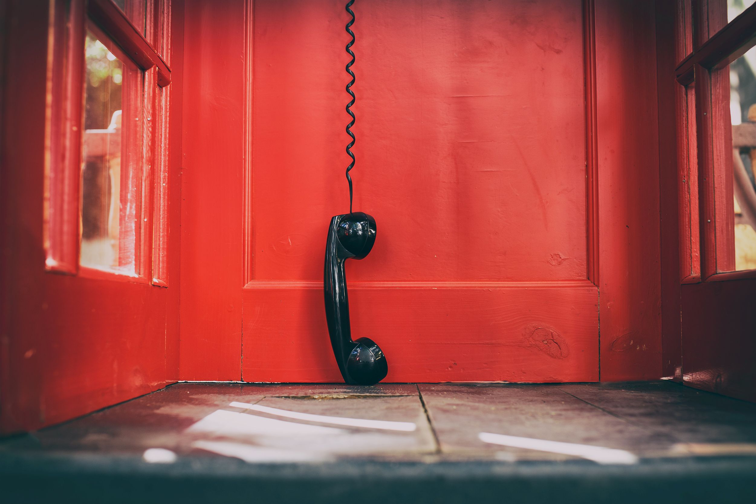 Black phone dangling by cord in phonebooth