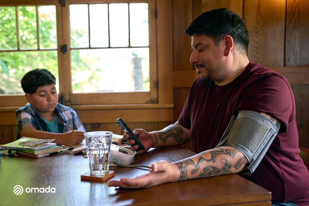 man wearing blood pressure cuff and looking at smartphone while sitting at table