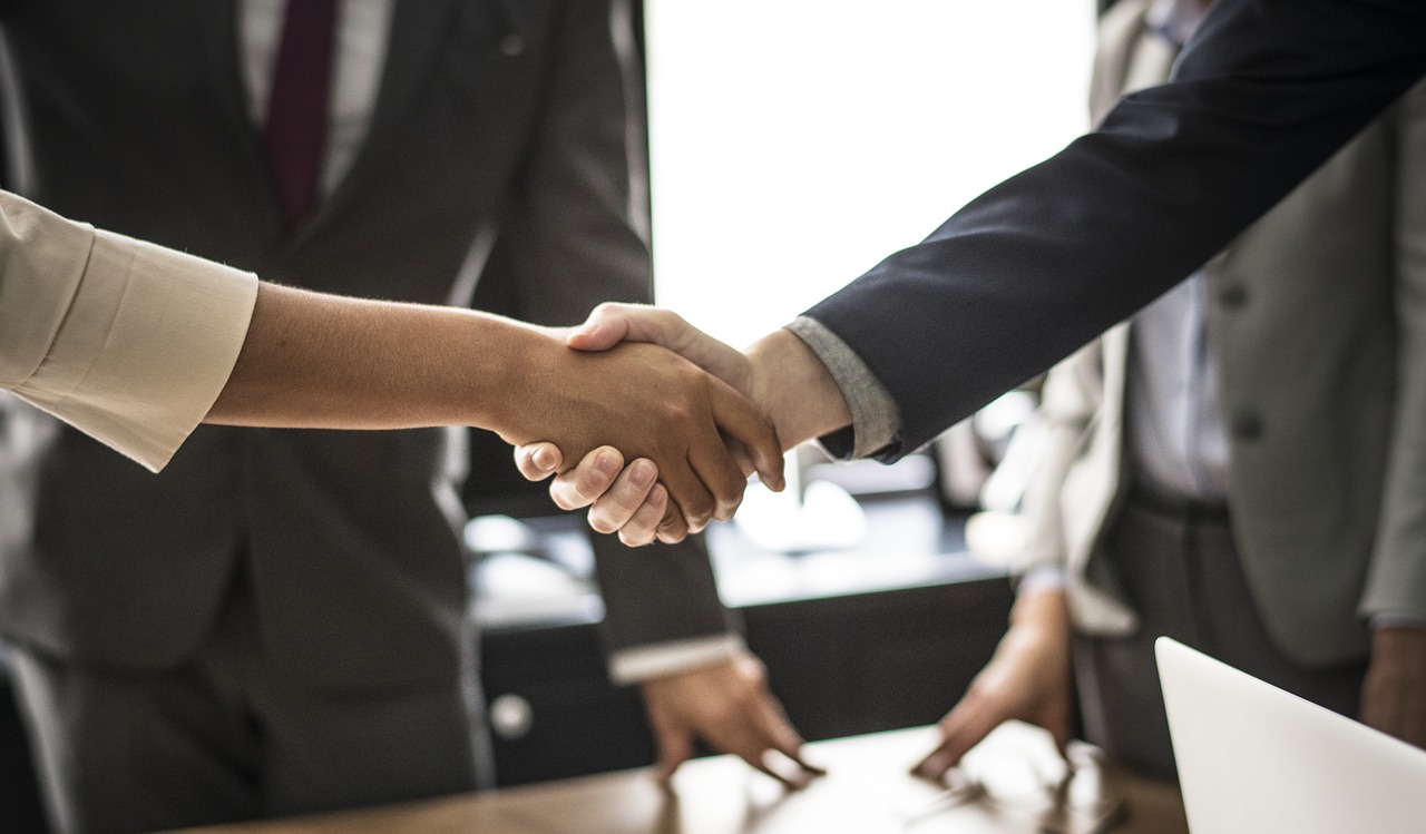 Close-up of two people shaking hands with other people in the background
