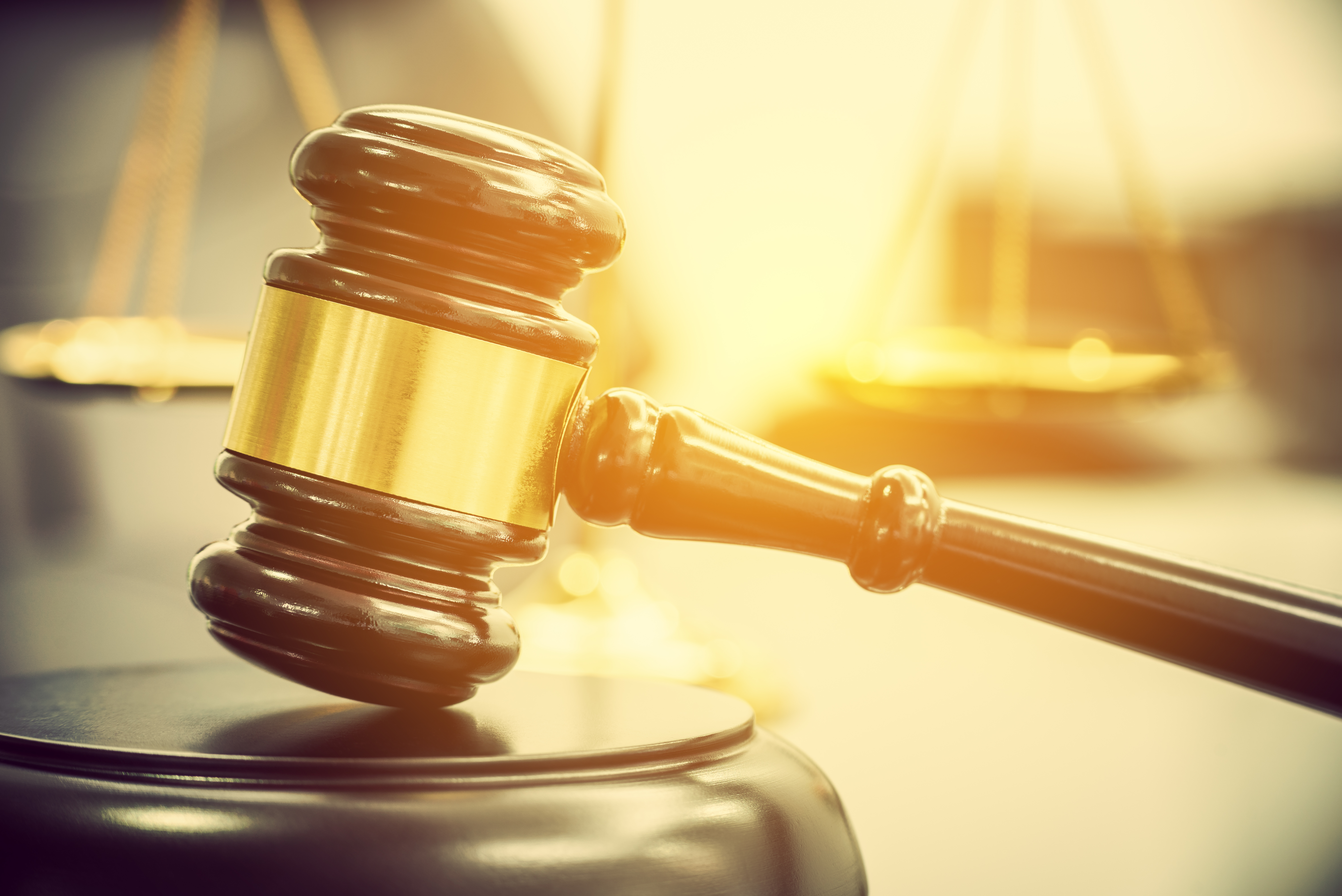 Wooden gavel and gold legal scale that appear to have sunlight falling on them